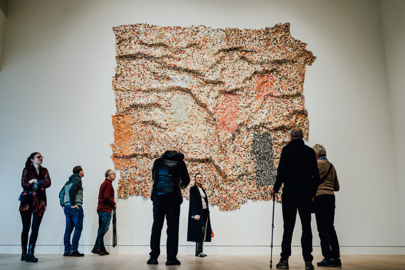 Besucher bewundern ein großes Gemälde, das in einem Kunstmuseum ausgestellt ist, und setzen sich mit dem Kunstwerk und miteinander auseinander.