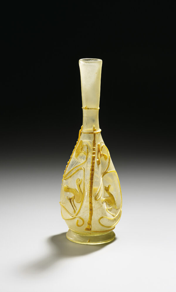 Unbekannt, Schlangenfadenflasche mit Wasservögeln, vermutlich Syrien, ca. 200–250 n. Chr., Entfärbtes durchscheinendes und gelbopakes Glas, frei geblasen, aufgelegte Fäden, Wandung gedrückt, (H x D): 21,6 × 7,2 cm: Schenkung, Foto: Kunstpalast, Düsseldorf