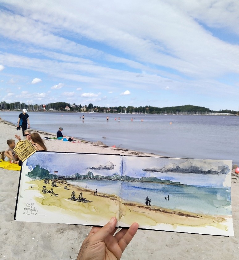 Eine Hand hält eine Aquarellskizze am Strand gegen die reale Strandszene und richtet die Zeichnung mit der Küstenlinie und den Menschen aus.