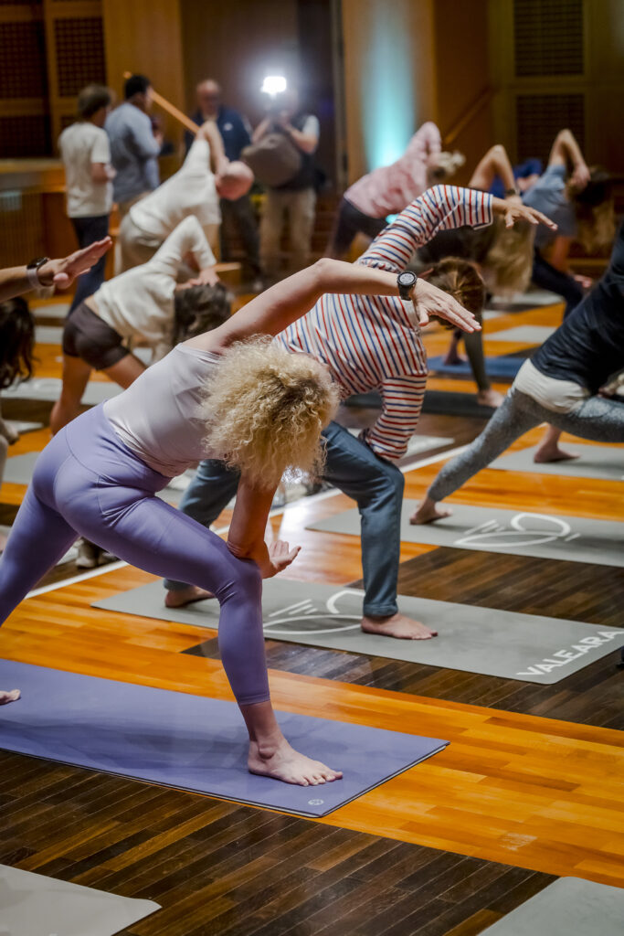 Menschen, die an einem Gruppen-Yoga-Kurs in einem beleuchteten Raum teilnehmen und sich seitlich auf Yogamatten dehnen.