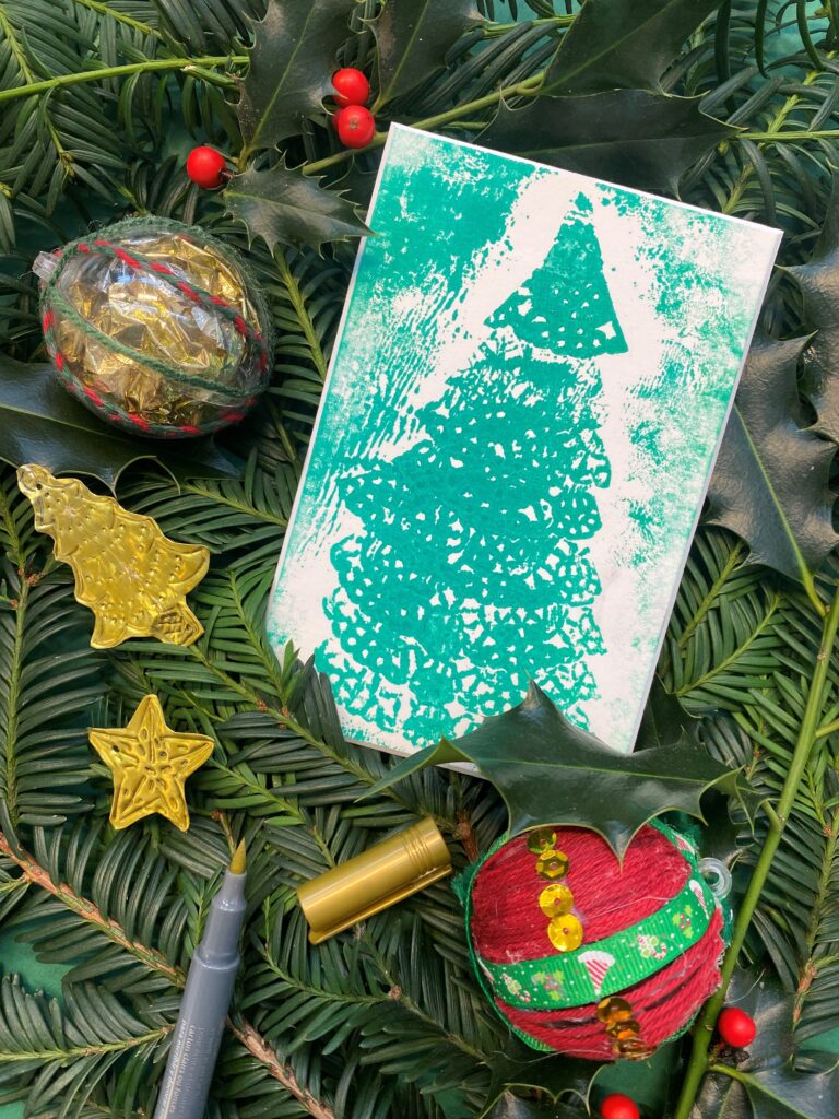 Eine handgefertigte grüne Weihnachtskarte mit einem Baumdesign, Ornamenten und Dekorationen auf Tannenzweigen.