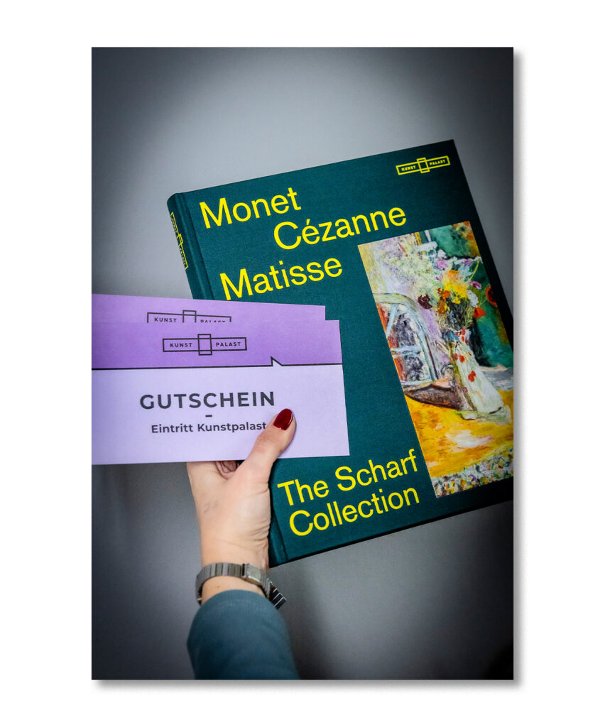 Eine Hand hält ein Monet-Cézanne-Matisse-Kunstbuch und zwei lila Kunstpalast-Eintrittsgutscheine.