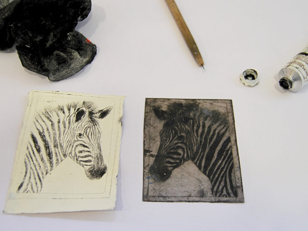 Auf einer weißen Fläche liegen ein Bleistift, eine Tintenröhre, ein Tuch und zwei Zebradrucke – einer auf weißem Papier, einer auf einer dunklen Radierplatte.